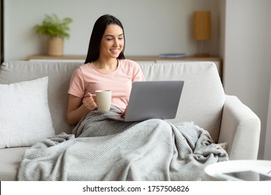 Weekend Leisure. Woman With Laptop Watching Movie Having Coffee Relaxing Sitting Covered With Blanket On Couch At Home