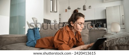 Weekend and lifestyle concept. Young woman lying on couch with digital tablet, scrolling social media, reading e-book or watching tv series on app.