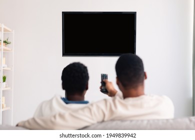 Weekend. Rear Back View Of African American Man And Woman Watching Tv, Guy Holding Remote Control, Changing Channels, Family Looking At Black Blank Television On Wall, Isolated Empty Monitor, Mock Up