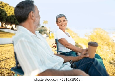 Weekend Vibes. Happy Senior Spouses Sitting In Chairs At Park Outside, Drinking Coffee From Paper Cups Enjoying Summer Day Together. Retirement Happiness And Relationship. Selective Focus - Shutterstock ID 2310519613