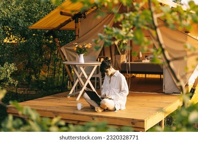 weekend work, Woman starts her morning working on a laptop while sitting near a tent in a glamping site for tourists - Powered by Shutterstock