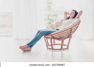 Weekends Finally! Relaxed Brunette Girl Is Sitting On Modern Chair Near The Window In Light Cozy Room At Home. She Is Enjoying Peace And Morning