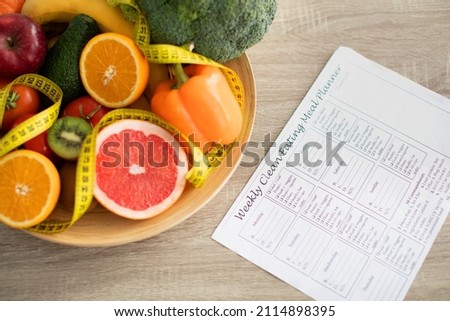 Weekly eating meal planner and plate of fresh fruits and vegetables nearby on table. Dietitian making healthy eating menu. Right nutrition and slimming concept