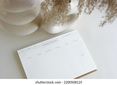 Weekly Planner Mockup With Copy Space On Home Desk Workspace With Modern Vase, Pen, Cup Coffee Top View On White Table.  Minimalist Lifestyle Neutral Colors.