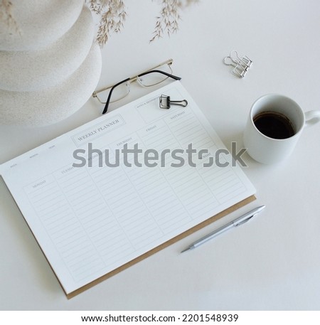 weekly planner mockup with copy space on home desk workspace with modern vase, pen, cup coffee top view on white table.  Minimalist lifestyle neutral colors.