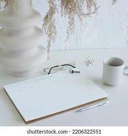 Weekly Planner On Home Desk Workspace With Modern Vase, Pen, Cup Coffee Top View On White Table.  Minimalist Lifestyle Neutral Colors.Copy Space