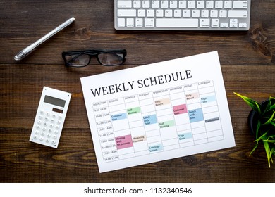 Weekly schedule of manager, office worker, pr specialist or marketing expert. Table with multicolored blocks on dark wooden office desk with computer, glasses, calculator top view