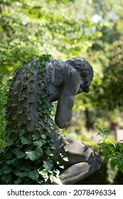 Weeping Sculpture With Overgrowing Ivy Leaves Growing On The Back. Head Bowed And In Hands Prayed. Leipzig, Germany