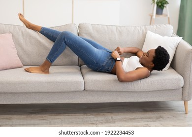 Weight Gain. Black Woman Struggling Zipping Too Small Skinny Jeans Lying On Sofa At Home. Gaining Excess Kilograms, Fat Belly And Visceral Fat Problem Concept