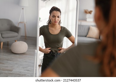 Weight Gain. Displeased Fit Woman Touching Fat Belly Looking In Mirror Standing At Home, Struggling To Lose Excess Weight After Unsuccessful Diet And Slimming. Selective Focus