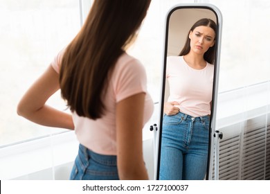 Weight Gain. Unhappy Girl Touching Drooping Belly Standing In Front Of Mirror At Home. Empty Space, Selective Focus - Shutterstock ID 1727100037