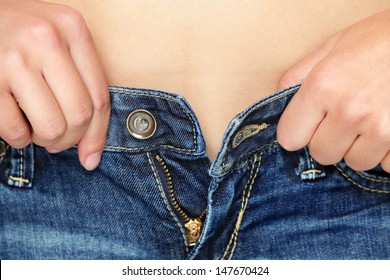 Weight Gain Woman Getting Dressed Wearing Jeans. Diet Concept - Closeup Of Women Hands Unable To Close The Pants Due To Gaining Fat On Hips. Fashion Girl Putting Pants On.