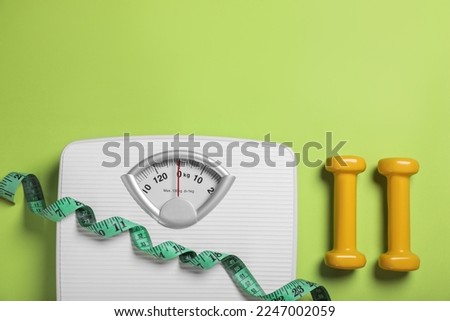 Weight loss concept. Scales, dumbbells and measuring tape on green background, flat lay. Space for text