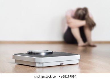 Weight loss fail concept. Scale and depressed, frustrated and sad woman sitting on floor holding head and arms on knees.