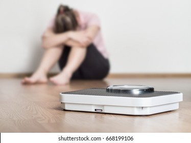 Weight loss fail concept. Scale and depressed, frustrated and sad woman sitting on floor holding head and arms on knees. - Shutterstock ID 668199106
