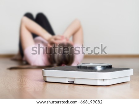 Weight loss fail concept. Scale and depressed, frustrated and sad woman lying on floor holding head and covering face with hands.
