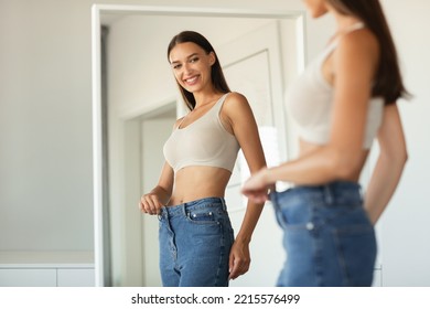 Weight Loss. Happy Lady Wearing Jeans After Slimming Comparing Size Before And After Dieting Posing Near Mirror Standing At Home. Cropped Shot, Selective Focus