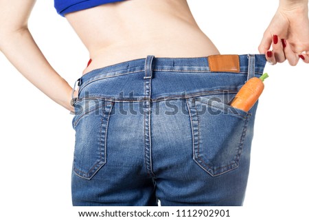 Weight loss and healthy eating or dieting concept. Slim girl in oversized jeans with a carrot in the pocket. Rear view. Close shot. Isolated on white background. 