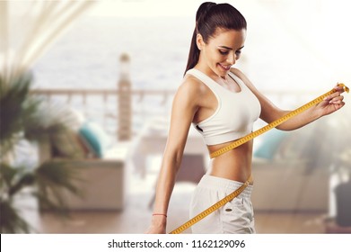 Weight loss, slim body, healthy lifestyle concept. Fit fitness girl measuring her waistline with measure tape on blue - Shutterstock ID 1162129096