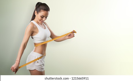 Weight Loss, Slim Body, Healthy Lifestyle Concept. Fit Fitness Girl Measuring Her Waistline With Measure Tape On Blue