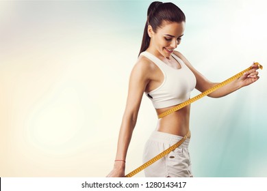 Weight loss, slim body, healthy lifestyle concept. Fit fitness girl measuring her waistline with measure tape on blue