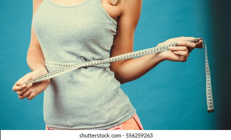 Weight loss, slim body, healthy lifestyle concept. Fit fitness girl measuring her waistline with measure tape on blue - Shutterstock ID 556259263