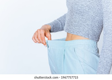 Weight Loss Young Woman Wearing Big Pants Showing Fat Reduction Around Her Waist, White Background.