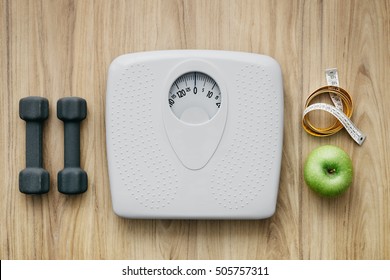 Weight scale, healthy snack, measuring tape and dumbbells on a table, weight loss and sports concept, flat lay