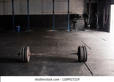 A weighted barbell sits in an empty warehouse gym. 