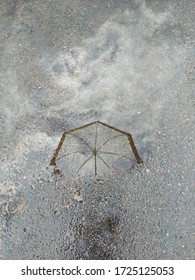 Weightless reflection of an umbrella and clouds in a puddle on the asphalt road