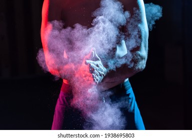 Weightlifter Claps Hands With Talcum Powder And Prepares For Workout In Red Blue Gradient Neon Light.