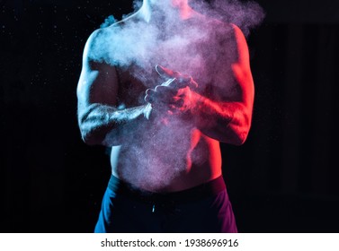 Weightlifter Claps Hands With Talcum Powder And Prepares For Workout In Red Blue Gradient Neon Light.