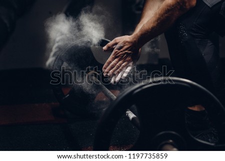 Weightlifter preparing for training workout lifter barbell. Hands in dust and talc. Dark background.