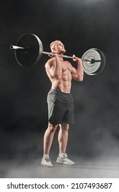 Weightlifting. A Male Weightlifter Lifts The Barbell With Effort. Professional Sport. Full Length Portrait On A Black Background With Smoke.