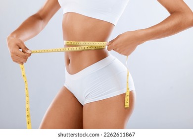 Weightloss, health and woman with measuring tape in a studio for her diet, exercise or wellness. Fitness, body and healthy slim female model checking the measurement of her waist by a gray background - Powered by Shutterstock