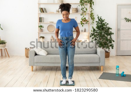 Weight-Loss Motivation. Smiling African Woman Weighing Herself After Successful Slimming And Weight Loss Standing On Scales Posing At Home. Full Length, Free Space For Text