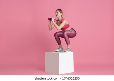 Weights exercises. Beautiful young female athlete practicing in studio, monochrome pink portrait. Sportive fit model training with jump box. Body building, healthy lifestyle, beauty and action concept