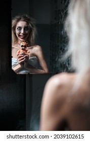 Weird Insane Girl With Creepy Ugly Doll In Abandoned Place (madhouse). Crazy Laughing Young Woman (freak) Looking Into Mirror. Portrait Of The Mental Sick (schizophrenic)