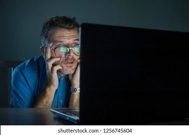 weird messy and stressed man in nerd glasses working in stress using internet on laptop computer late night in the dark looking stupid and ridiculous as nerdy worker problem on isolated background