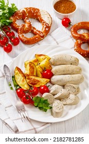 Weisswurst, Bavarian White Sausage Of Minced Veal, Pork Back Bacon, Spices And Parsley On White Plate With Roast Potato, Fresh Tomatoes, Soft Pretzels, Sweet Mustard, Vertical View From Above