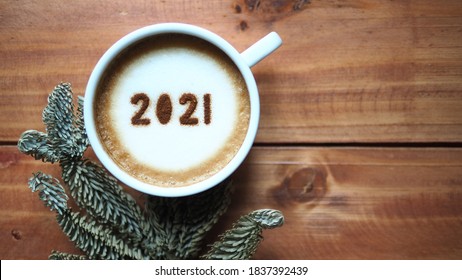 Welcome 2021 Theme Coffee Cup With Number 2021 On Frothy Surface Flat Lay On Wooden Table Background With Dried Pine Branches. Happy New Year 2021, Holidays Food Art Concept. (close Up, Top View)