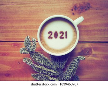 Welcome 2021 Theme Coffee Cup With Number 2021 On Frothy Surface Flat Lay On Wooden Table Background With Dried Pine Branches. Happy New Year 2021, Holidays Food Art Concept. (close Up, Top View)