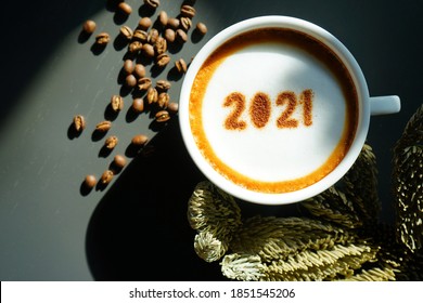 Welcome 2021 Theme Coffee Cup With Number 2021 On Frothy Surface Flat Lay On Grey Wooden Table With Coffee Beans And Dried Pine Branches. Happy New Year 2021, Holidays Food Art Concept. (close Up)