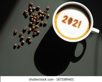 Welcome 2021 Theme Coffee Cup With Number 2021 On Frothy Surface Flat Lay On Grey Wooden Table With Coffee Beans. Happy New Year 2021, Holidays Food Art Concept. (top View, Space For Text)