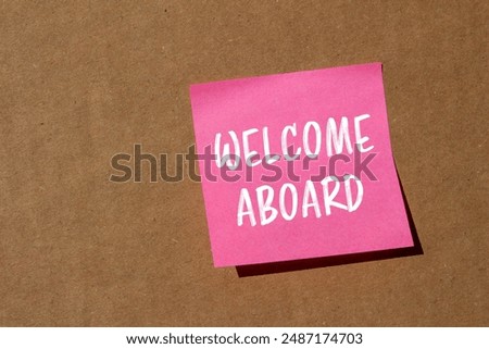 Welcome aboard message written on pink paper with cardboard background. Conceptual welcome aboard symbol. Copy space.