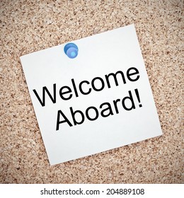 Welcome Aboard Typed Onto A Yellow Note And Pinned To A Cork Notice Board. A Phrase Used To Welcome A New Employee Or Team Member.