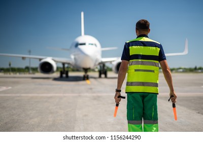 Welcome Back. Back View Of Airport Worker Meeting Passenger Aircraft