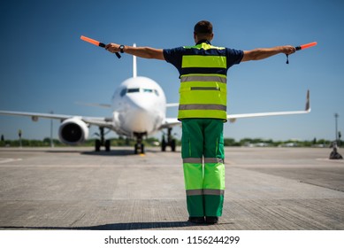 Welcome Back. Back View Of Airport Worker Looking At Passenger Plane And Signaling