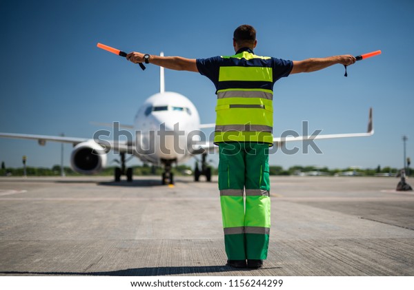 Welcome back. Back view of airport worker\
looking at passenger plane and\
signaling
