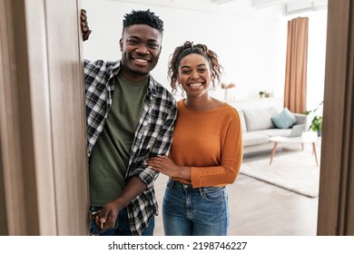 Welcome. Cheerful Black Couple Opening Entry Door Smiling To Camera Posing Standing At Home. Real Estate Buyers Meeting You In Modern Living Room Indoor. New House Ownership Concept - Powered by Shutterstock